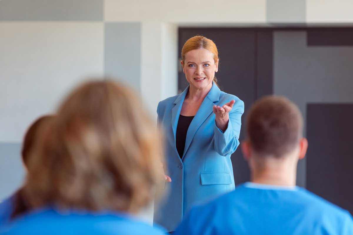 A woman with red hair and a bright blue blazer facilitates a compliance training session.