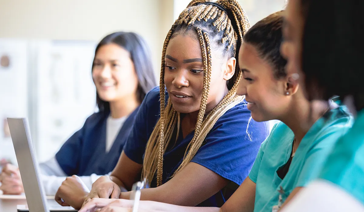 A group of nursing students are sitting at a table looking at a laptop. Find out what implicit bias training is and where to find a training program to meet your nursing  licensing requirements.